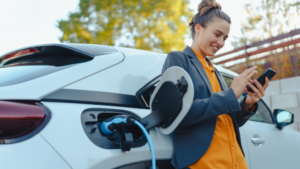 A woman leaning on her car while waiting for it to charge at an EV charging station