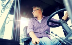 farming, agriculture and people concept - senior man driving tractor at farm