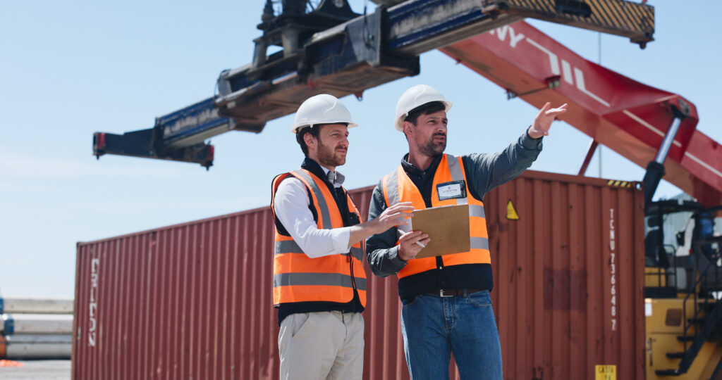 Men, shipping team and clipboard at container yard for supply chain, inspection or pointing. People, workers and planning shipment at dock for freight, logistics checklist or export cargo in industry.