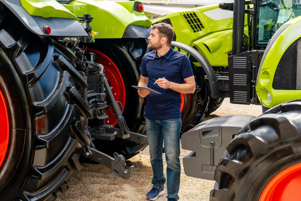 Buyer in a navy polo carefully inspecting the rear of a large green tractor at an equipment dealership