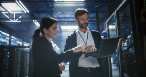 IT professionals reviewing server equipment on a laptop inside a data center