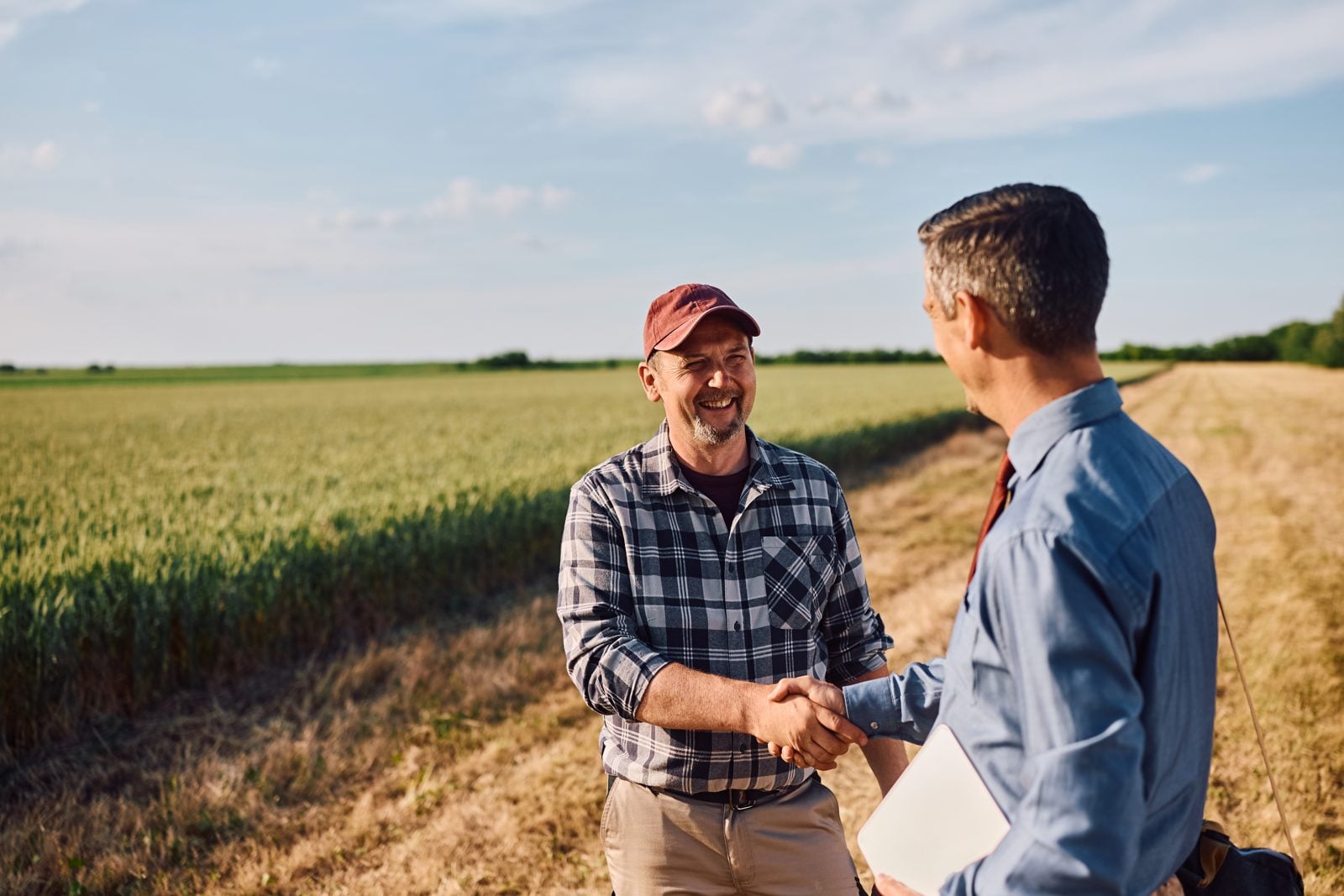 Farmer in a plaid shirt shaking hands with a financing advisor next to a wheat field