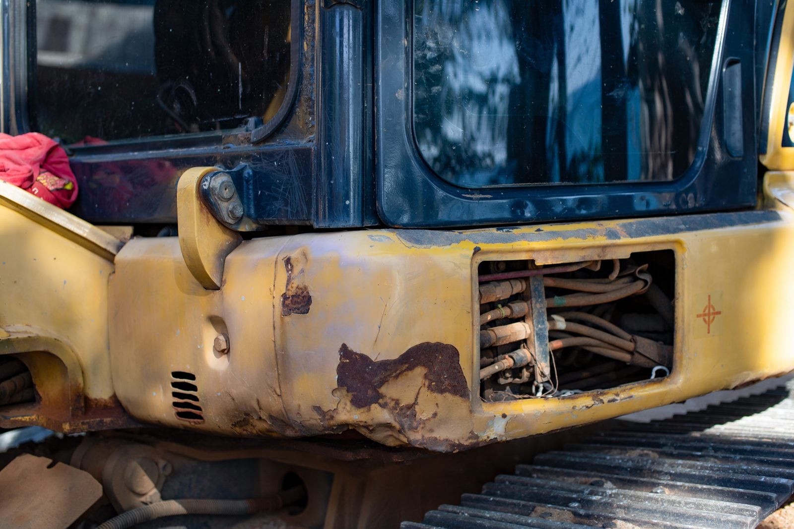 Close-up of a worn yellow excavator with rust and exposed hydraulic lines